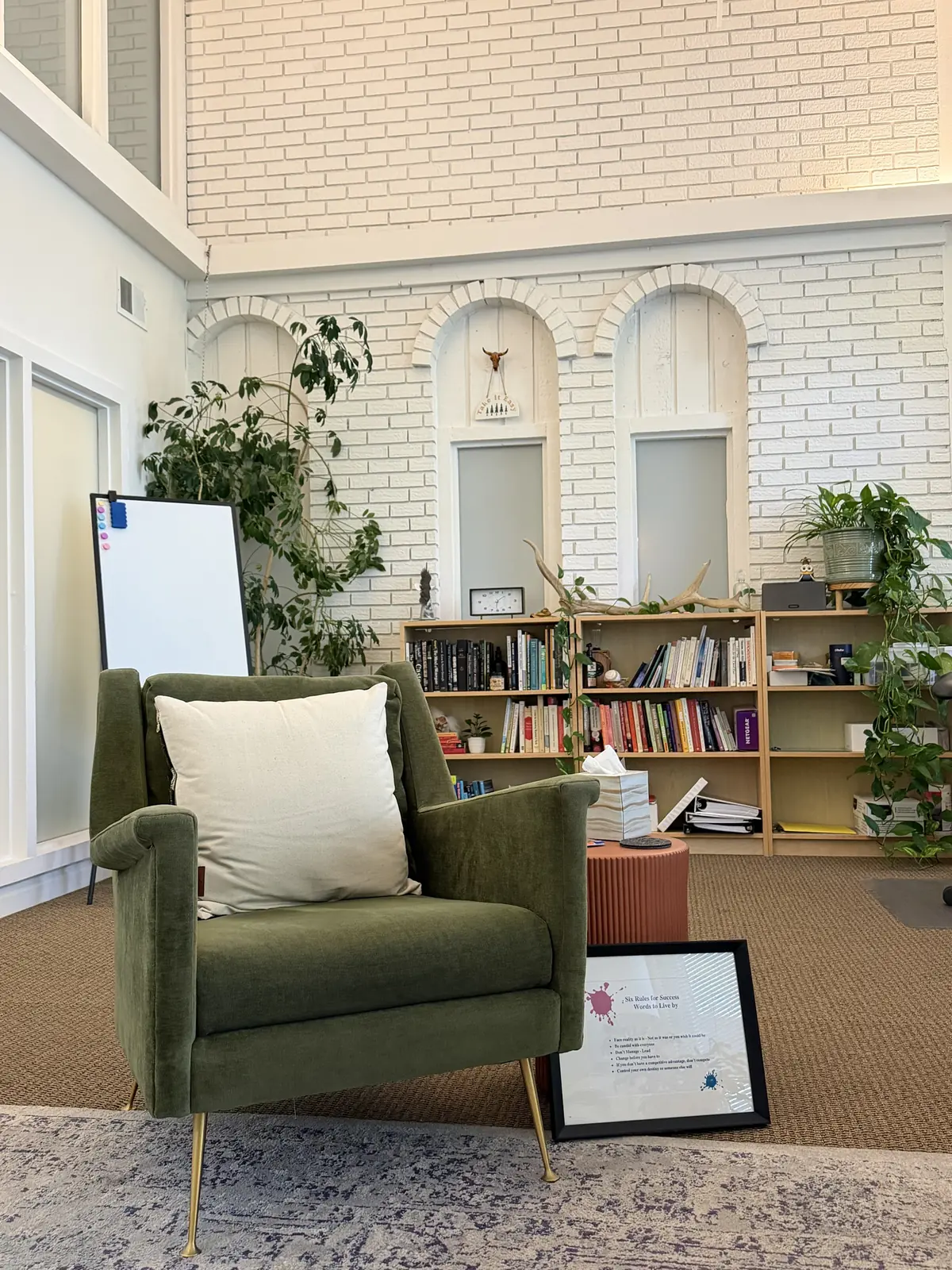A therapy office with a green armchair, plants, and bookshelves.